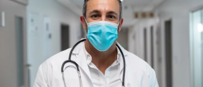 Retrato de un médico mestizo con mascarilla de pie en el pasillo del hospital.