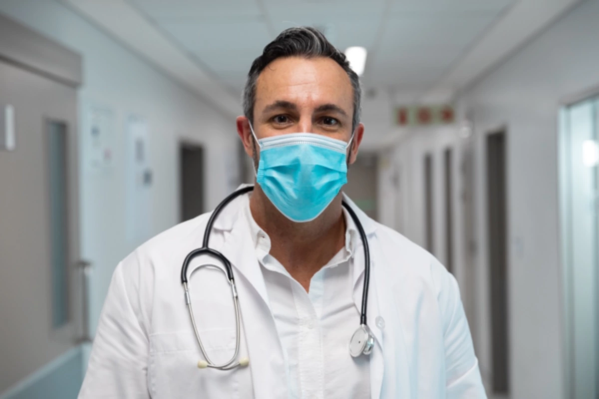 Retrato de un médico mestizo con mascarilla de pie en el pasillo del hospital.