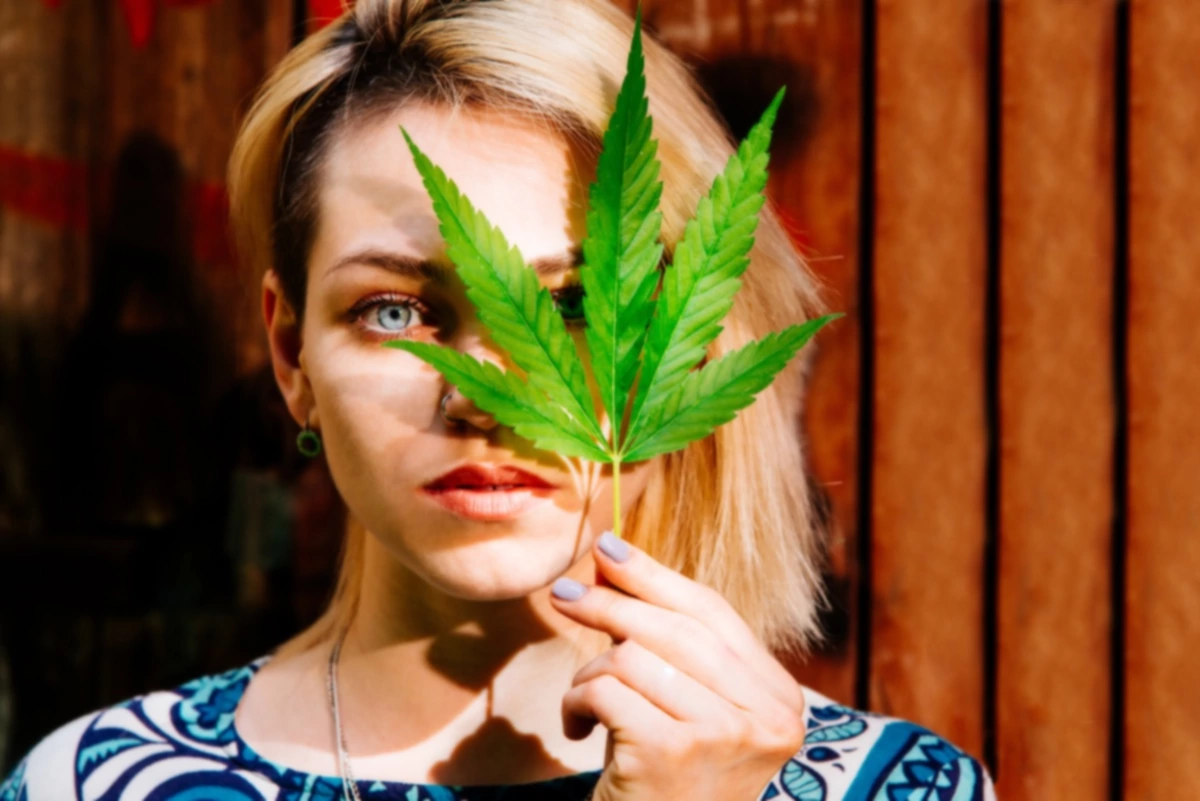 Mujer con una hoja de cannabis delante de la cara.