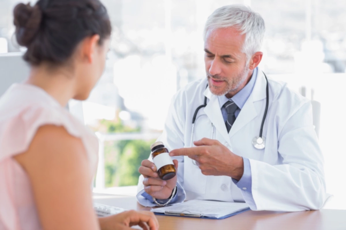 Médico explicando el frasco de pastillas al paciente en la oficina en el escritorio