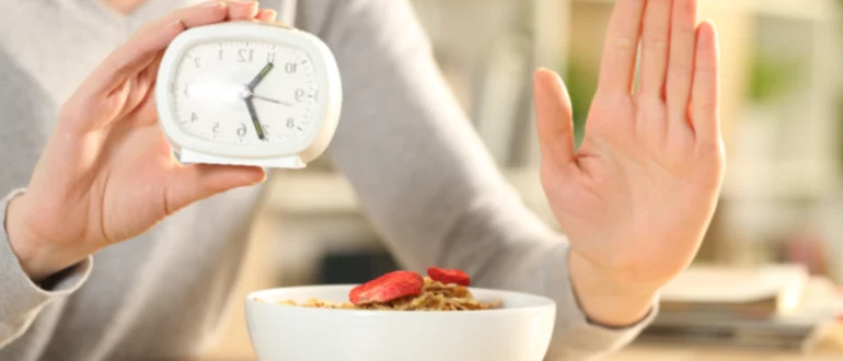 mujer sosteniendo la mano y el reloj mostrando el concepto de ayuno intermitente con un tazón de cereales