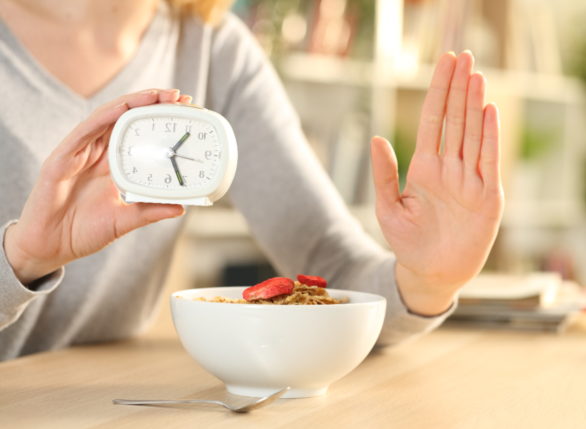 mujer sosteniendo la mano y el reloj mostrando el concepto de ayuno intermitente con un tazón de cereales