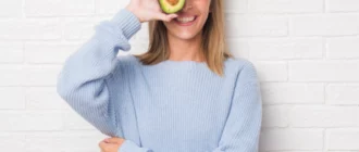 Beautiful,Young,Woman,Over,White,Brick,Wall,Eating,Fresh,Avocado