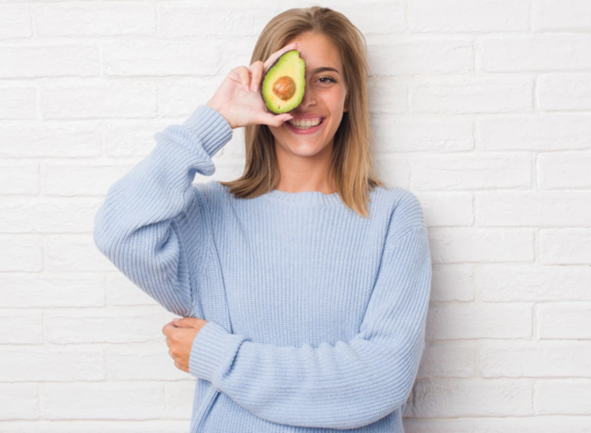 Beautiful,Young,Woman,Over,White,Brick,Wall,Eating,Fresh,Avocado